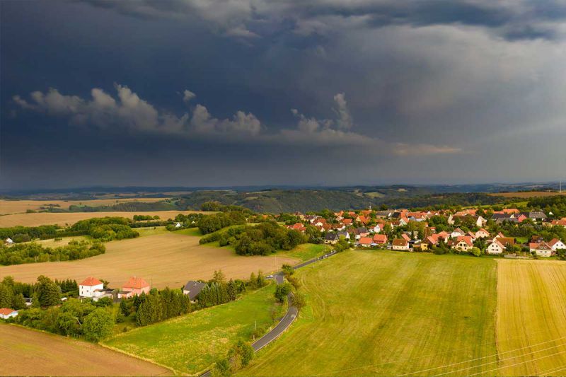 Luftaufnahme eines kleinen Dorfes mit Feld im Vordergrund