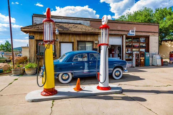 Blaues Auto steht vor einer alten Tankstelle.