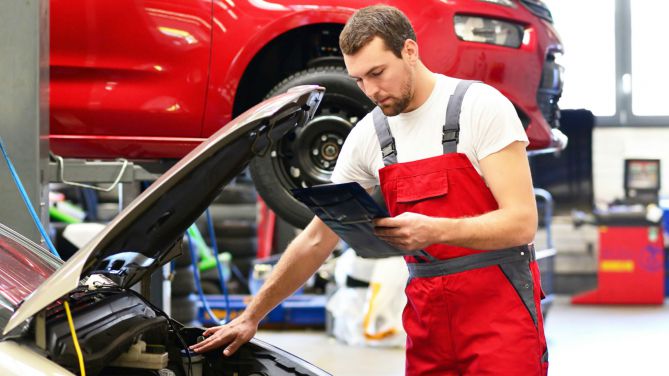 Kfz-Mechaniker schaut in der Werkstatt unter die Motorhaube eines Autos.