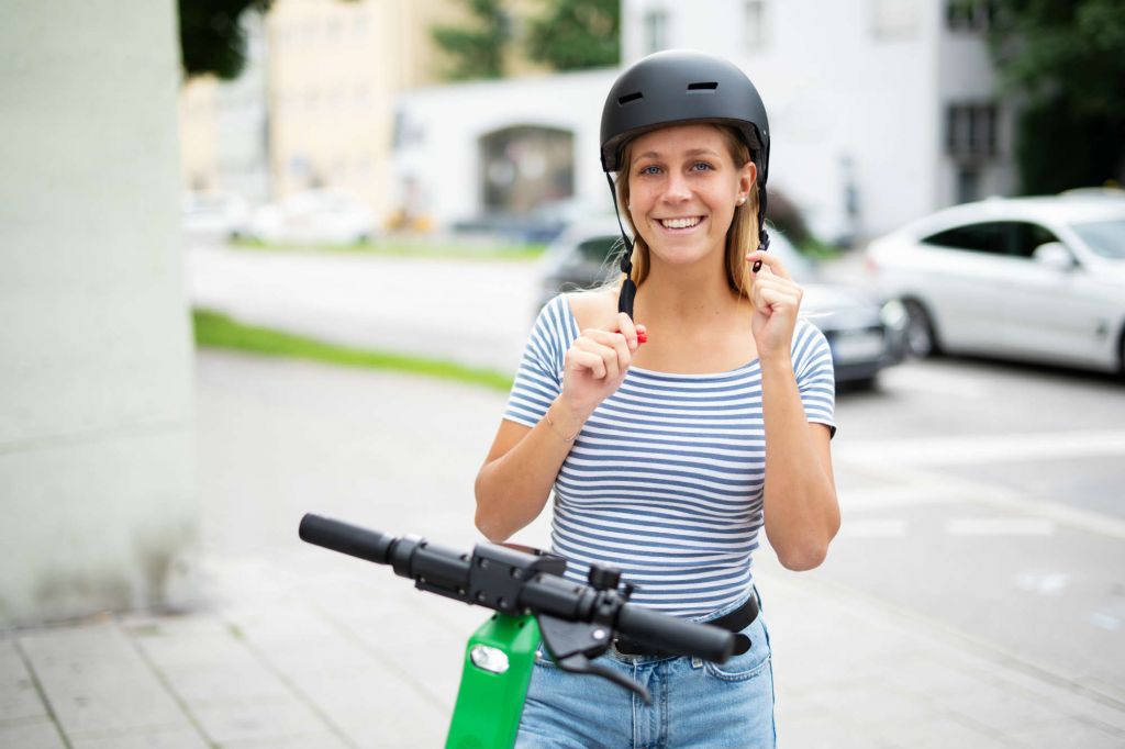Frau mit Helm auf einem E-Scooter.