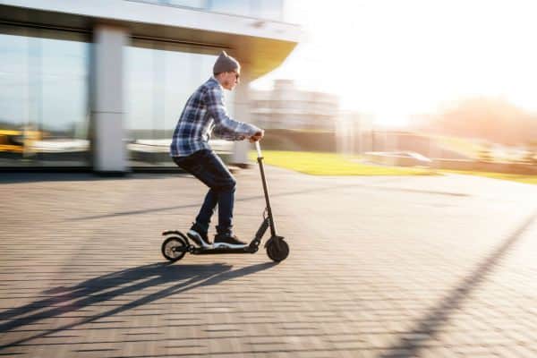 Mann mit Mütze und Sonnenbrille fährt auf einem E-Scooter.