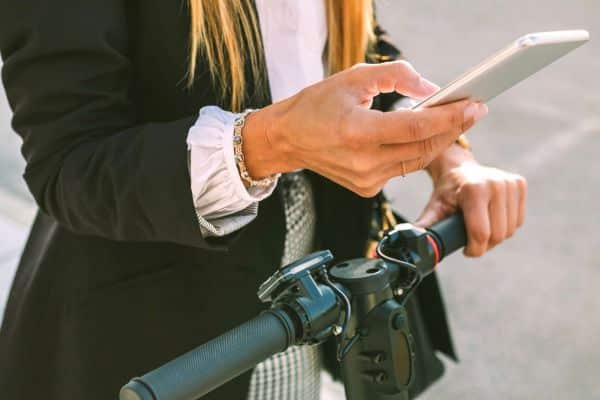 Frau auf E-Scooter mit Smartphone in der Hand.