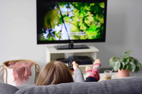 Junge Frau schaut Fernsehen und sitzt auf einem grauen Sofa