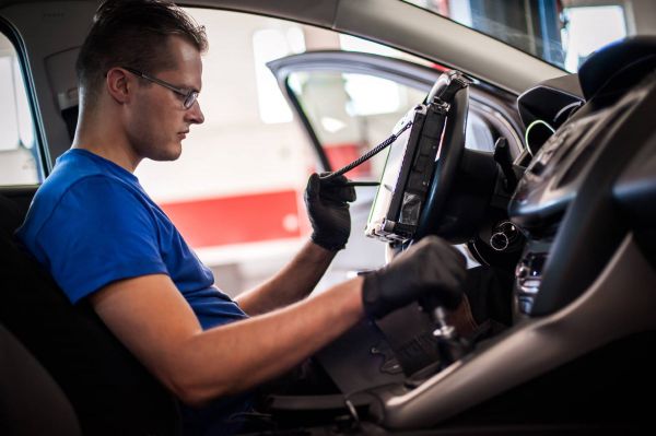 Mechaniker prüft mit einem Prüf-Gerät die Software des Elektroautos