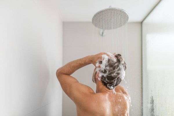 Mann wäscht Haare mit niedrigerem Wasserdruck