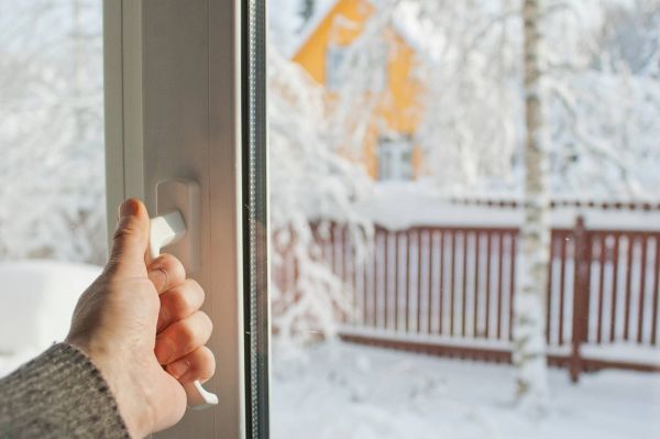 Hand an einem Fenstergriff, im Hintergrund winterliche, schneebedeckte Landschaft.
